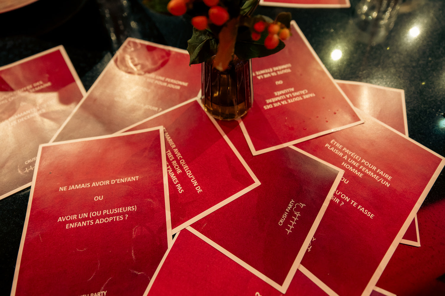 Cartes de jeu 'Tu préfères' disposées sur une table avec un vase de fleurs, lors d'une soirée Crush Party. Cartes rouges avec des questions pour briser la glace et animer les interactions entre célibataires.
