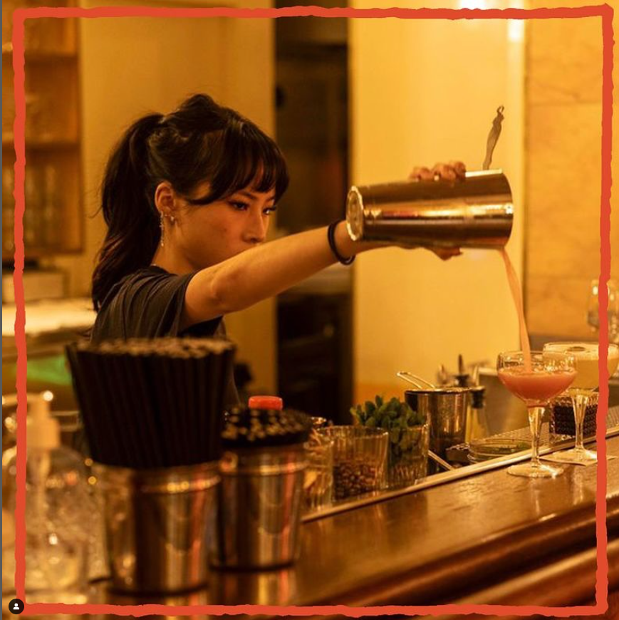 Barmaid préparant un cocktail lors d'une soirée Crush Party dans un bar intimiste, ambiance chaleureuse et festive.