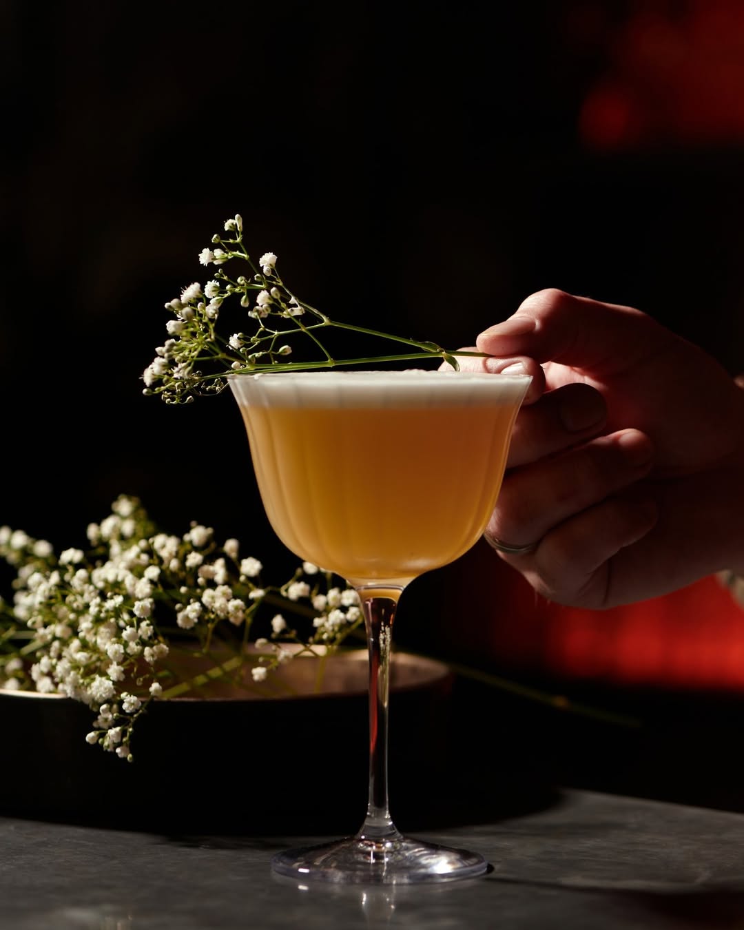 Main tenant un cocktail raffiné décoré de fleurs blanches au Kube Hotel à Paris, boisson signature dans une ambiance élégante.