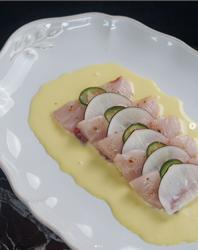 Assiette gastronomique avec des tranches de poisson cru, décorées de fines rondelles de radis et de concombre, servies sur une sauce jaune crémeuse. Plat raffiné proposé lors des dîners Crush Party dans des restaurants partenaires comme Bazurto Paris.